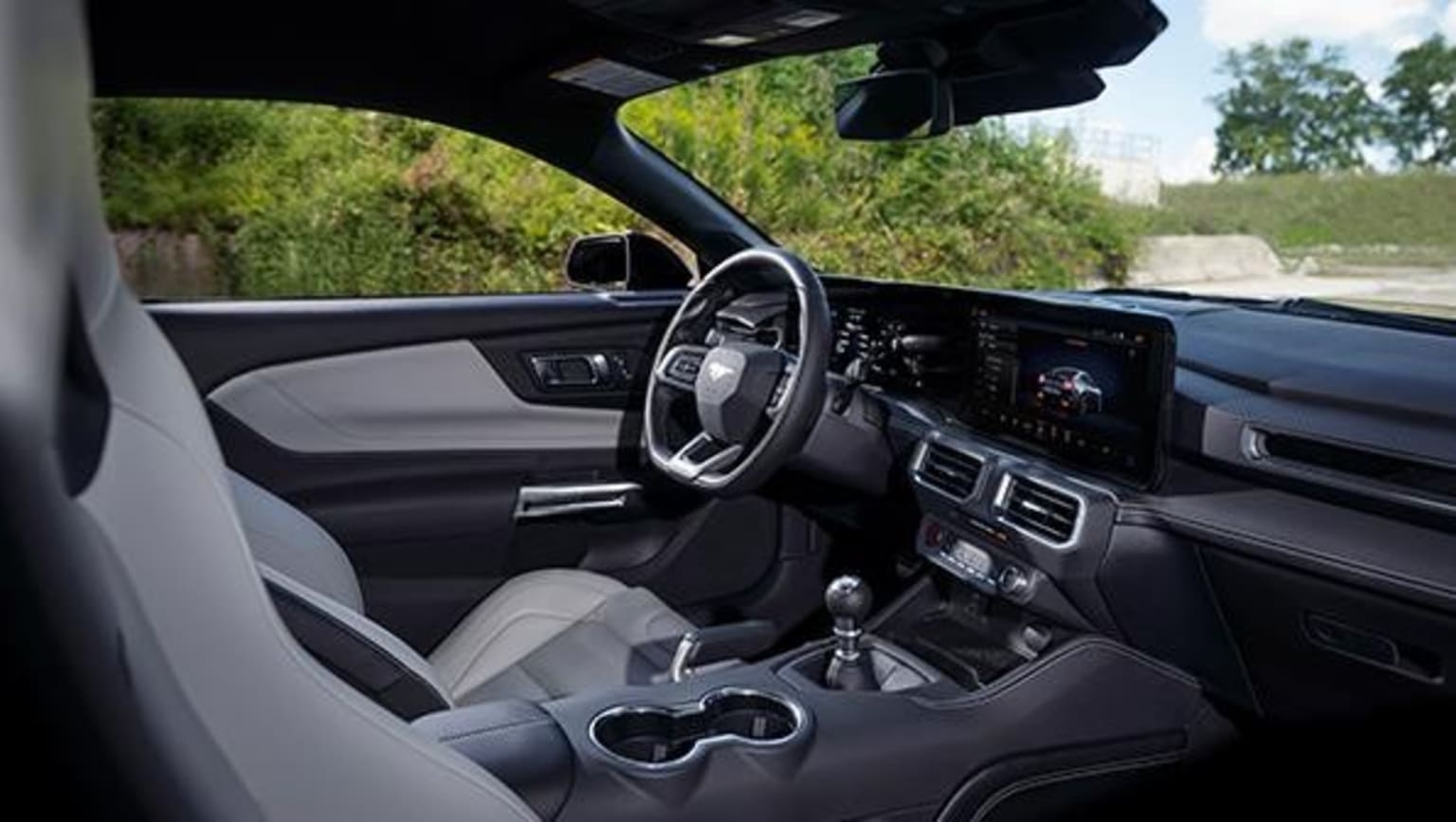 Interior of a modern vehicle with steering wheel, dashboard, and center console, with lush greenery visible through the windshield.