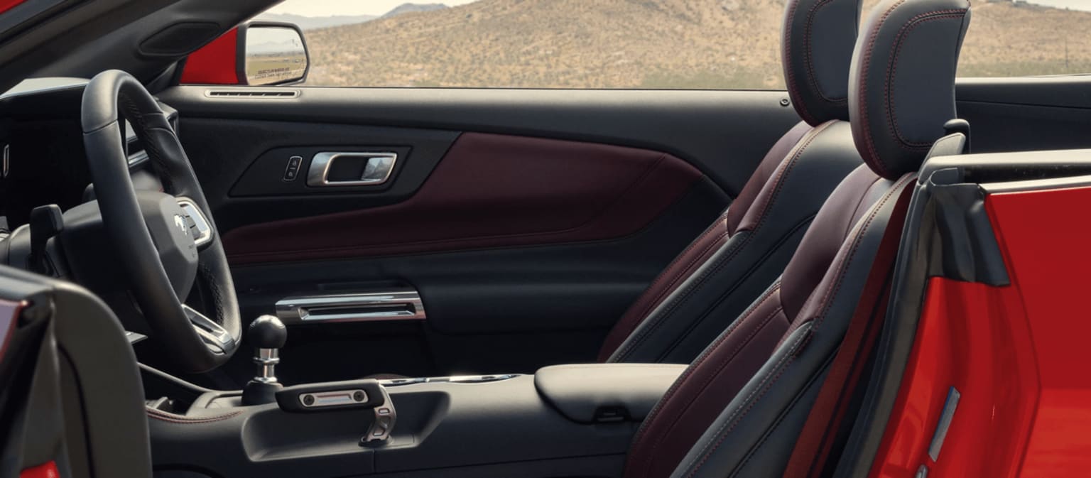 The image displays the interior of a vehicle with a mountainous landscape visible through the windshield in the background. The foreground shows the vehicle's dashboard and seats with a sleek and modern design.
