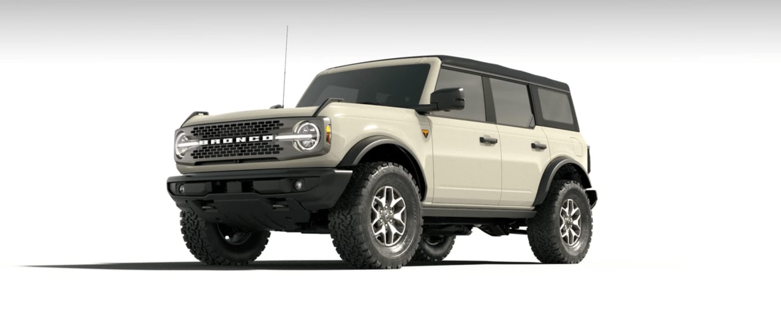 Off-road vehicle with a boxy, angular design and large, knobby tires in the foreground against a plain, light-colored background.