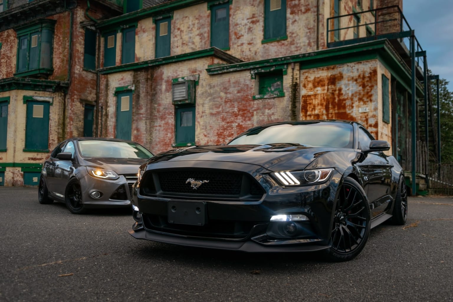 a black mustang parked in front of a building with green shuttered windows and a rusted metal door