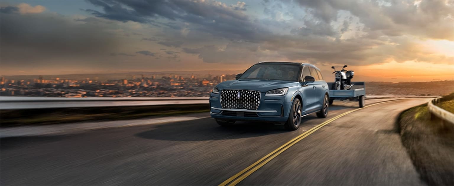 2025 Lincoln Corsair towing capacity being used to tow a motorcycle on a trailer up a hill overlooking the city at sunset