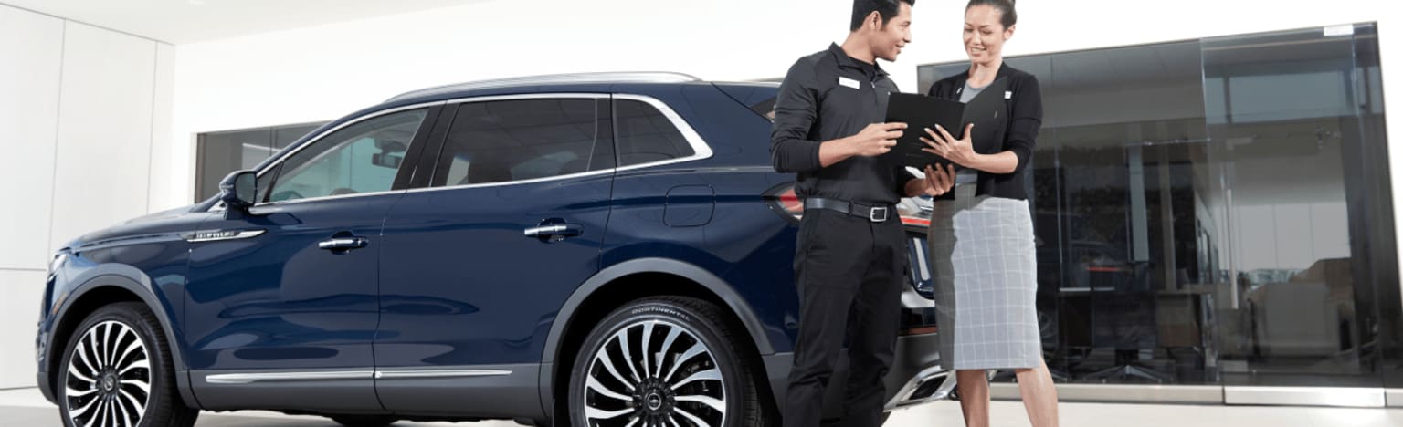 A dark blue SUV parked next to a man and woman in a showroom.
