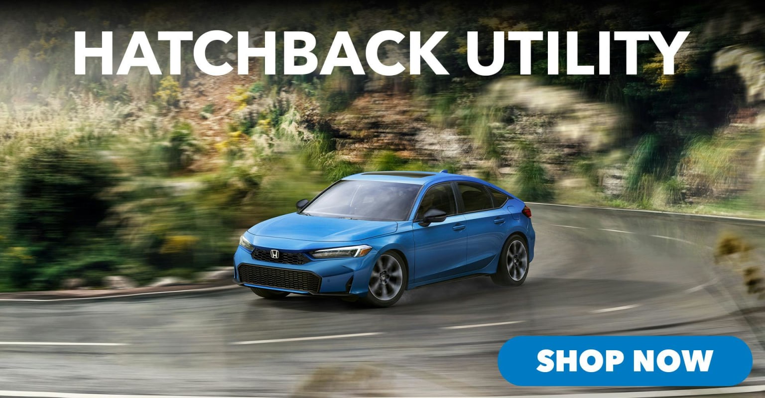 A blue hatchback utility vehicle driving on a wet road with a blurred hillside in the background.