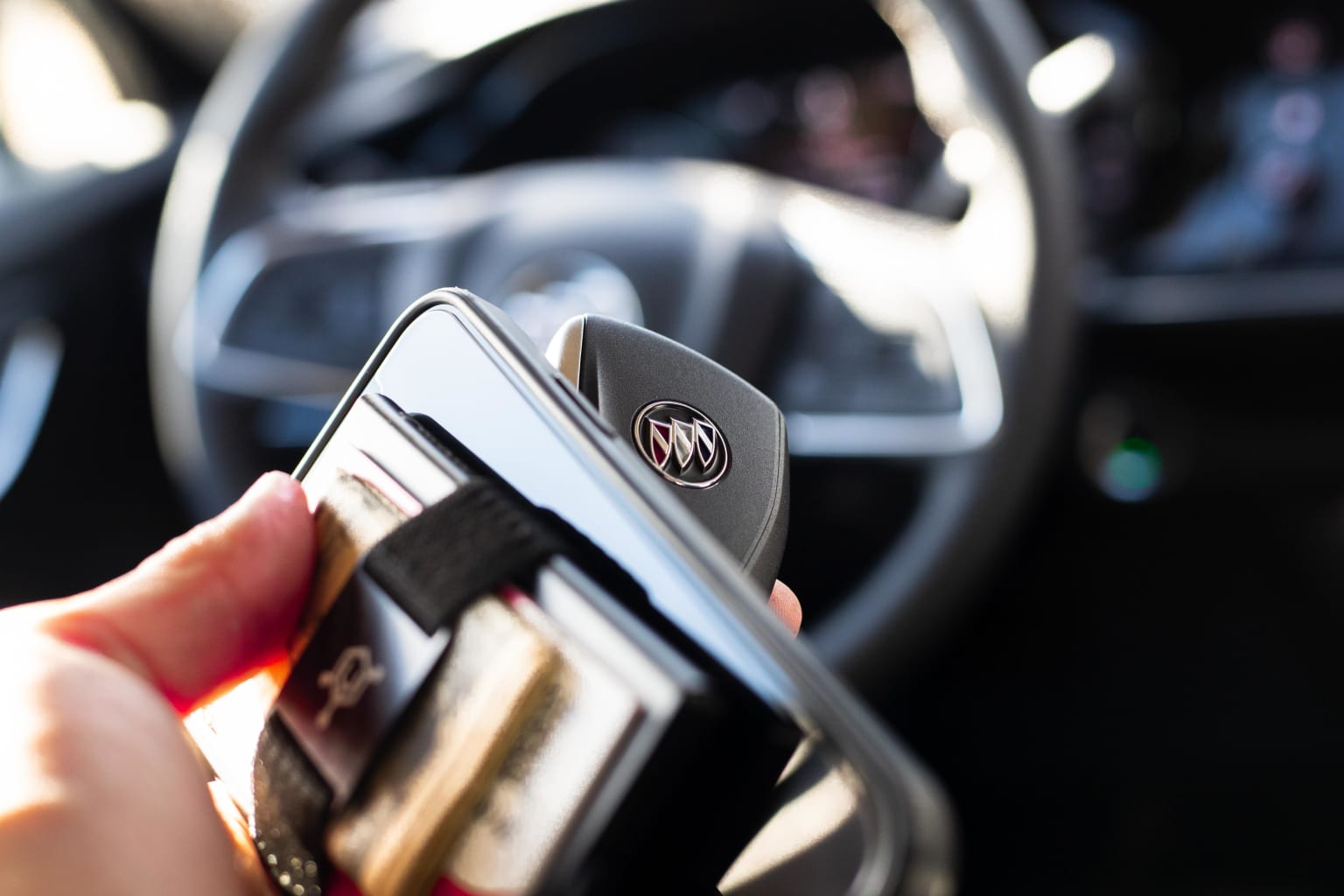 a person holding a cell phone in their hand while sitting in a car with a steering wheel in the background