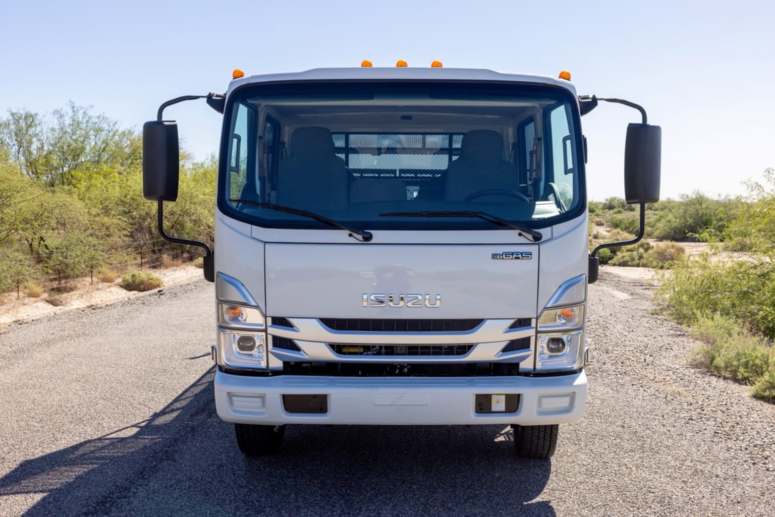 A white truck is parked on a gravel road with dry brush and trees in the background under a clear blue sky.