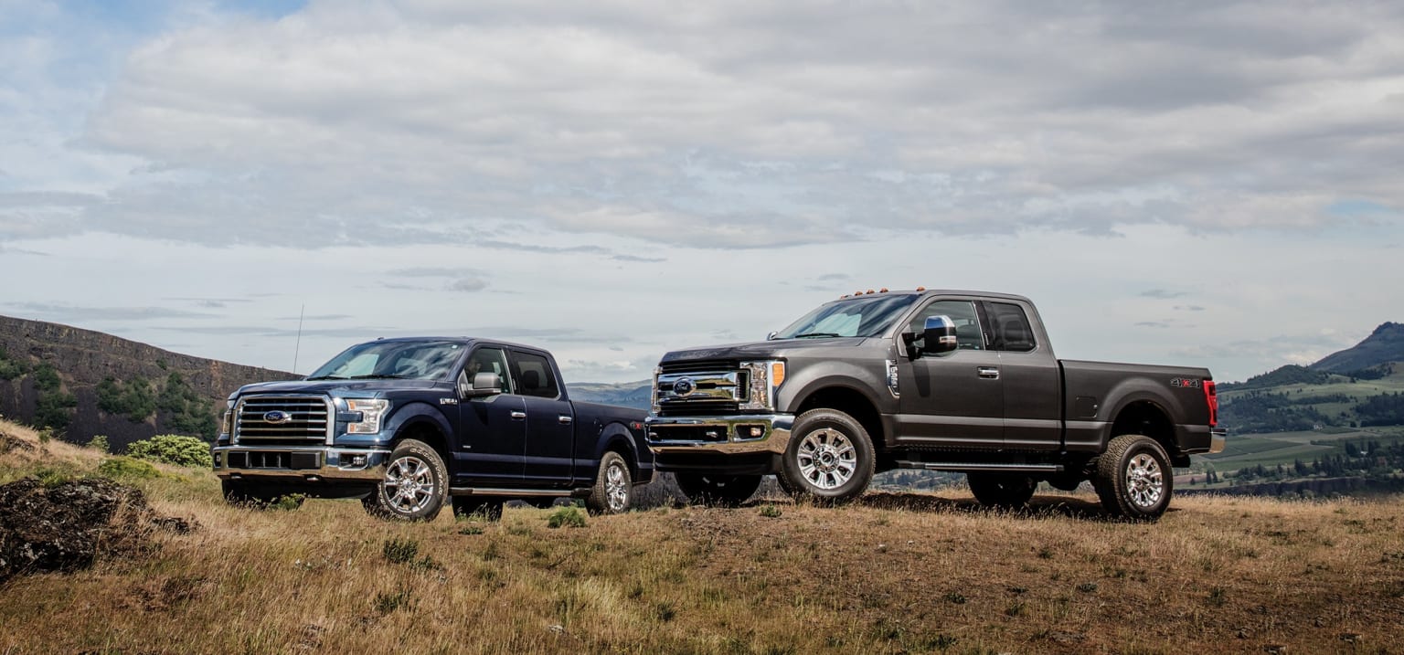 a couple of trucks parked on top of a grass covered hill next to a hill covered with trees and bushes