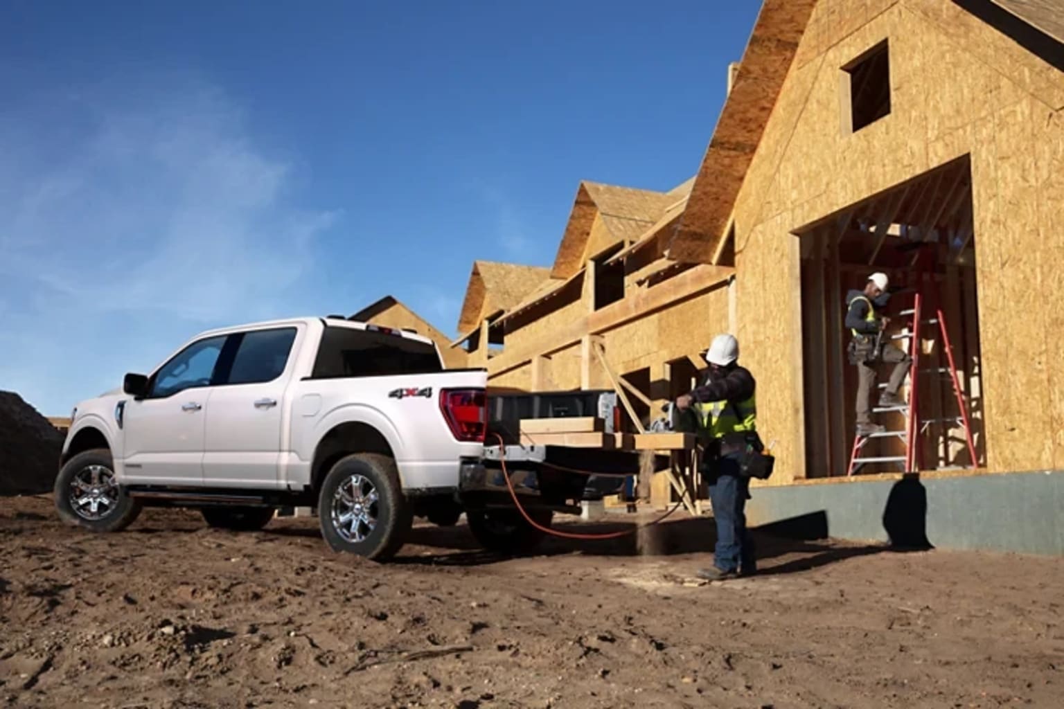 a white truck parked in front of a house under construction with a man working on the back of the truck