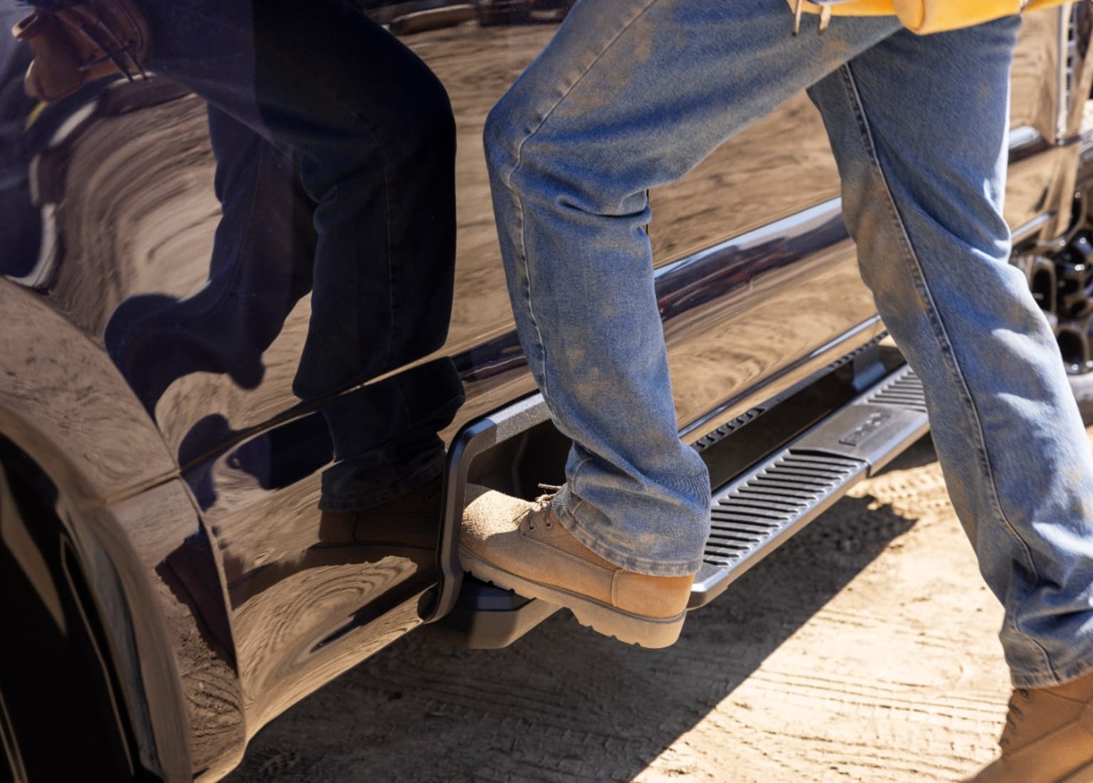 a pair of men standing on the side of a vehicle with their feet on the door step of the vehicle