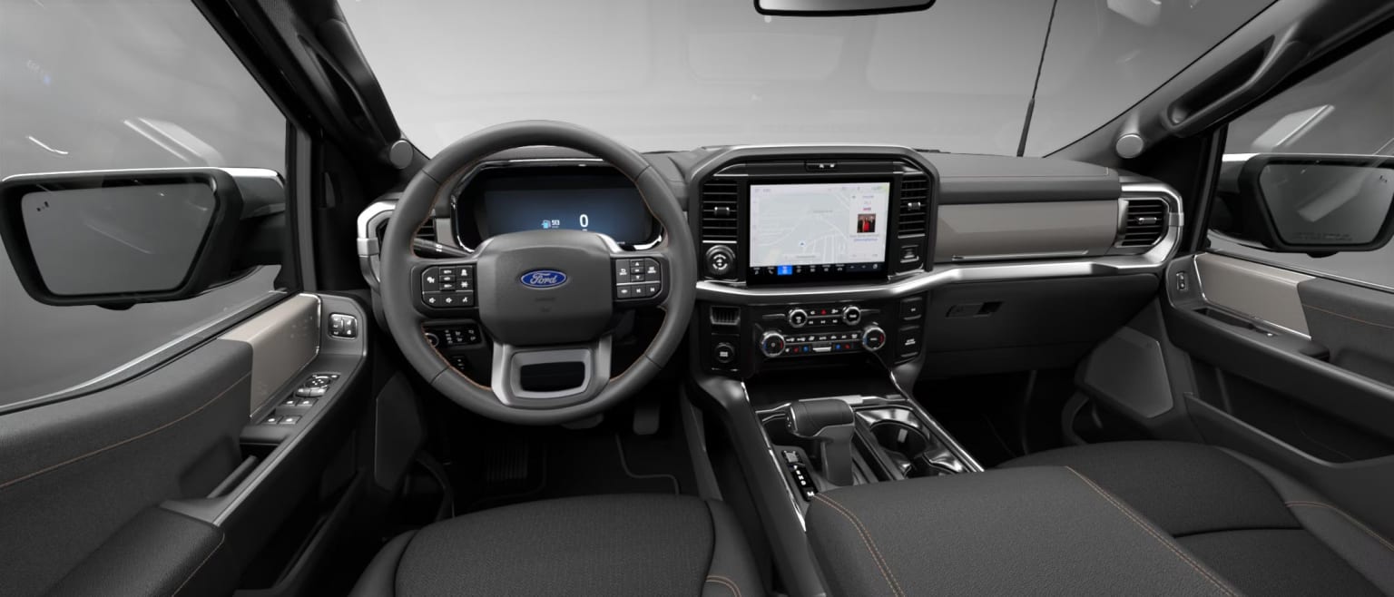 Interior of a vehicle with a steering wheel, dashboard, and various controls and displays visible against a neutral, monochromatic background.