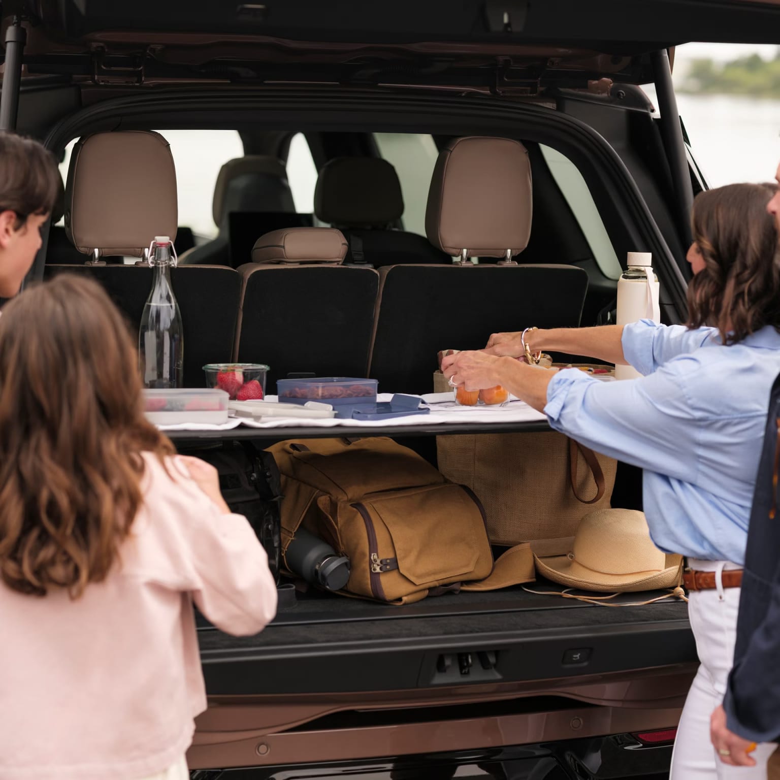The image shows the interior of a vehicle with the rear cargo area visible, several people are seated in the vehicle, and various items such as bags and hats can be seen in the cargo area.