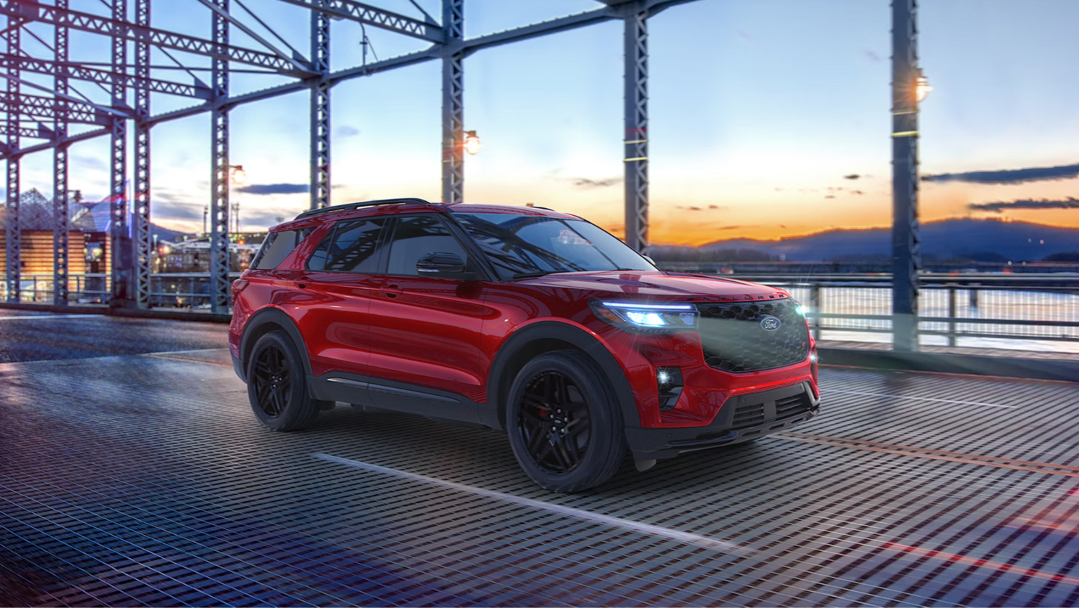 A red SUV parked on a metal grate platform beneath a blue industrial bridge during sunset.