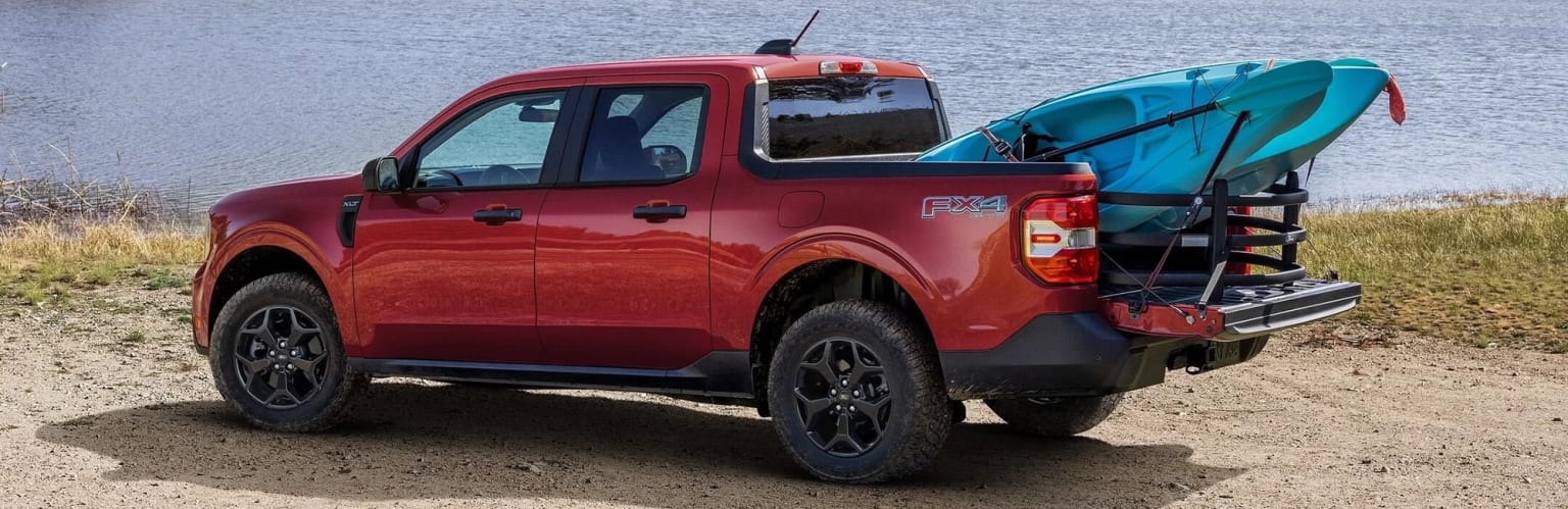 A red four-wheel-drive pickup truck parked on a sandy beach, with a body of water visible in the background.