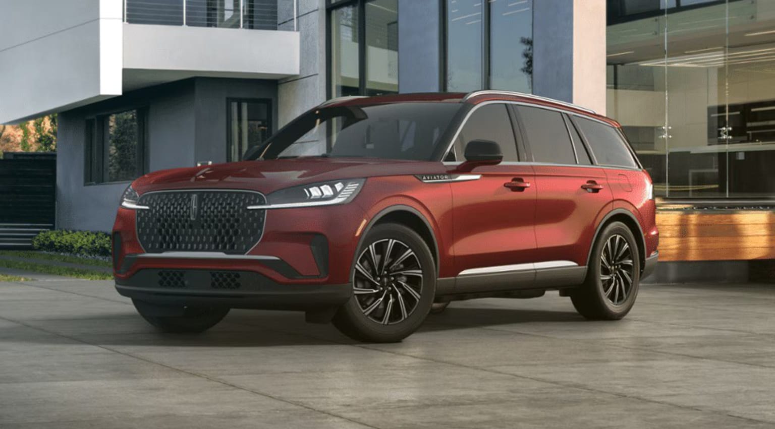 A large, red SUV with a distinctive grille design parked in front of a modern, glass-fronted building.
