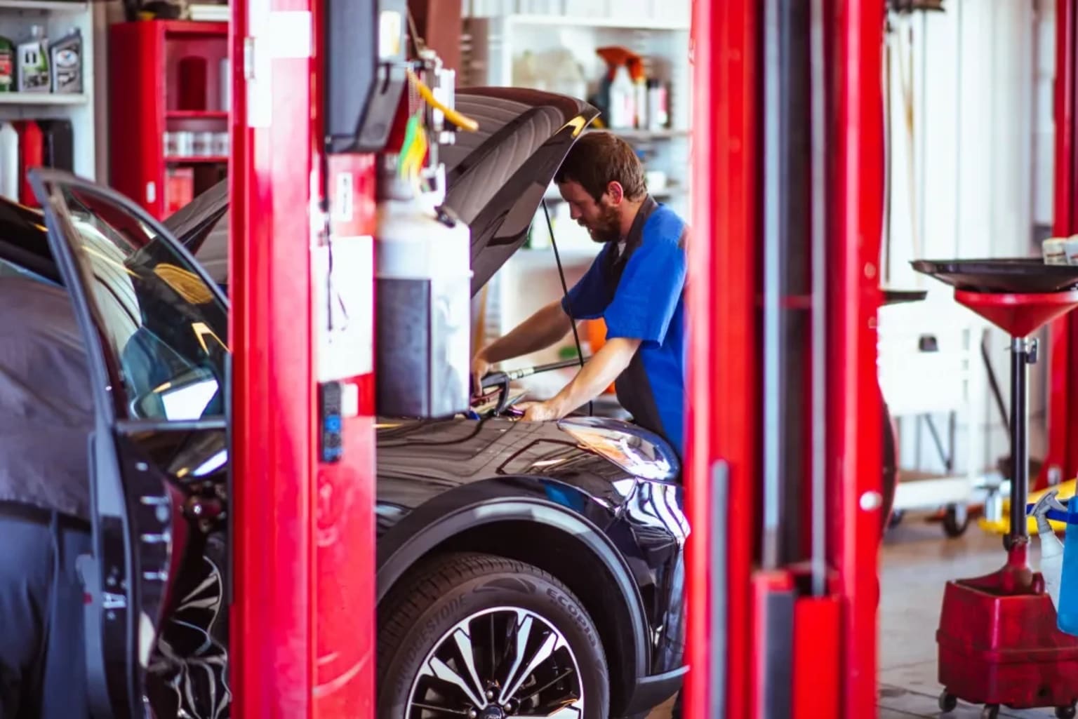 A person working on a car in an auto repair shop, surrounded by various tools and equipment.