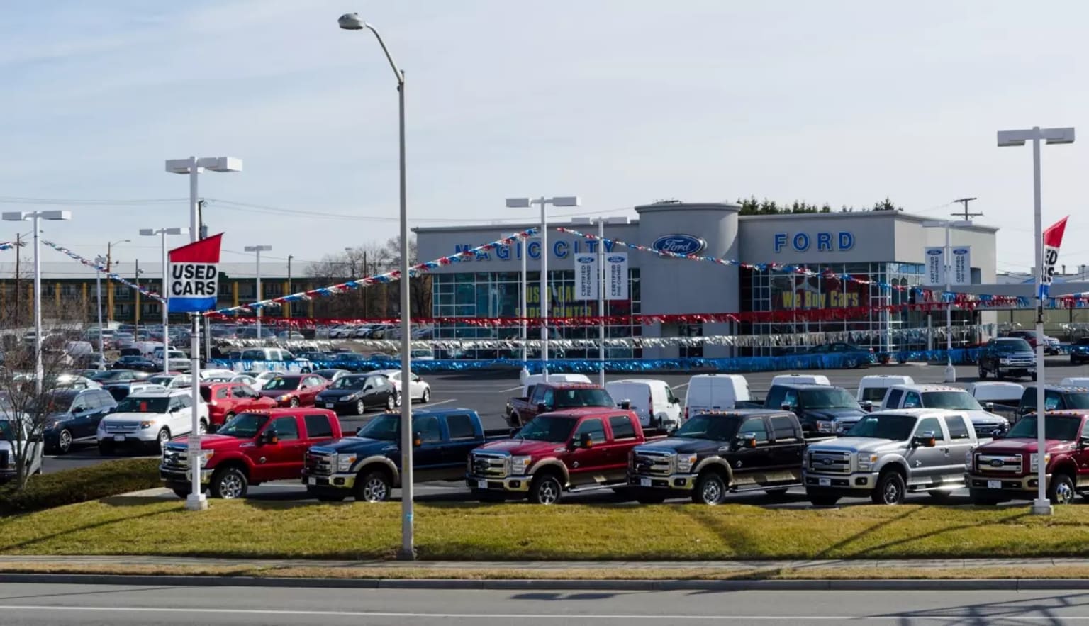 a parking lot full of trucks parked in front of a ford dealership with flags flying in the background