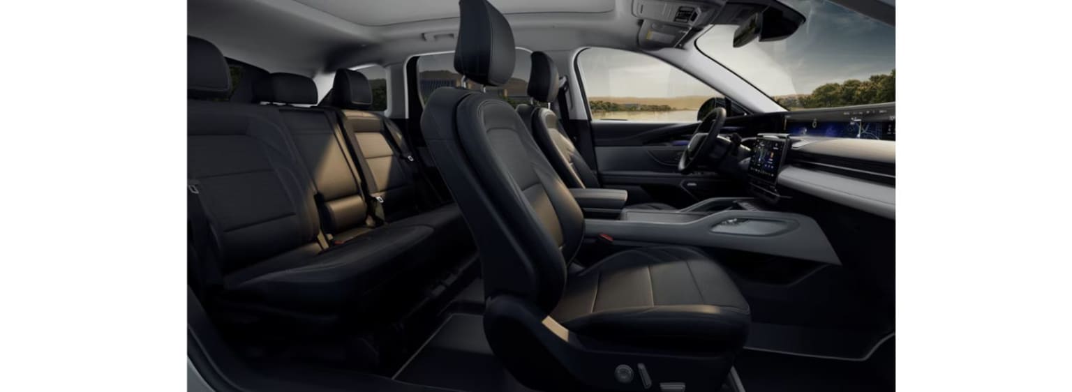 Interior of a vehicle with black leather seats and a dashboard featuring various controls and displays. Background outside the vehicle is a scenic landscape with a body of water and trees.