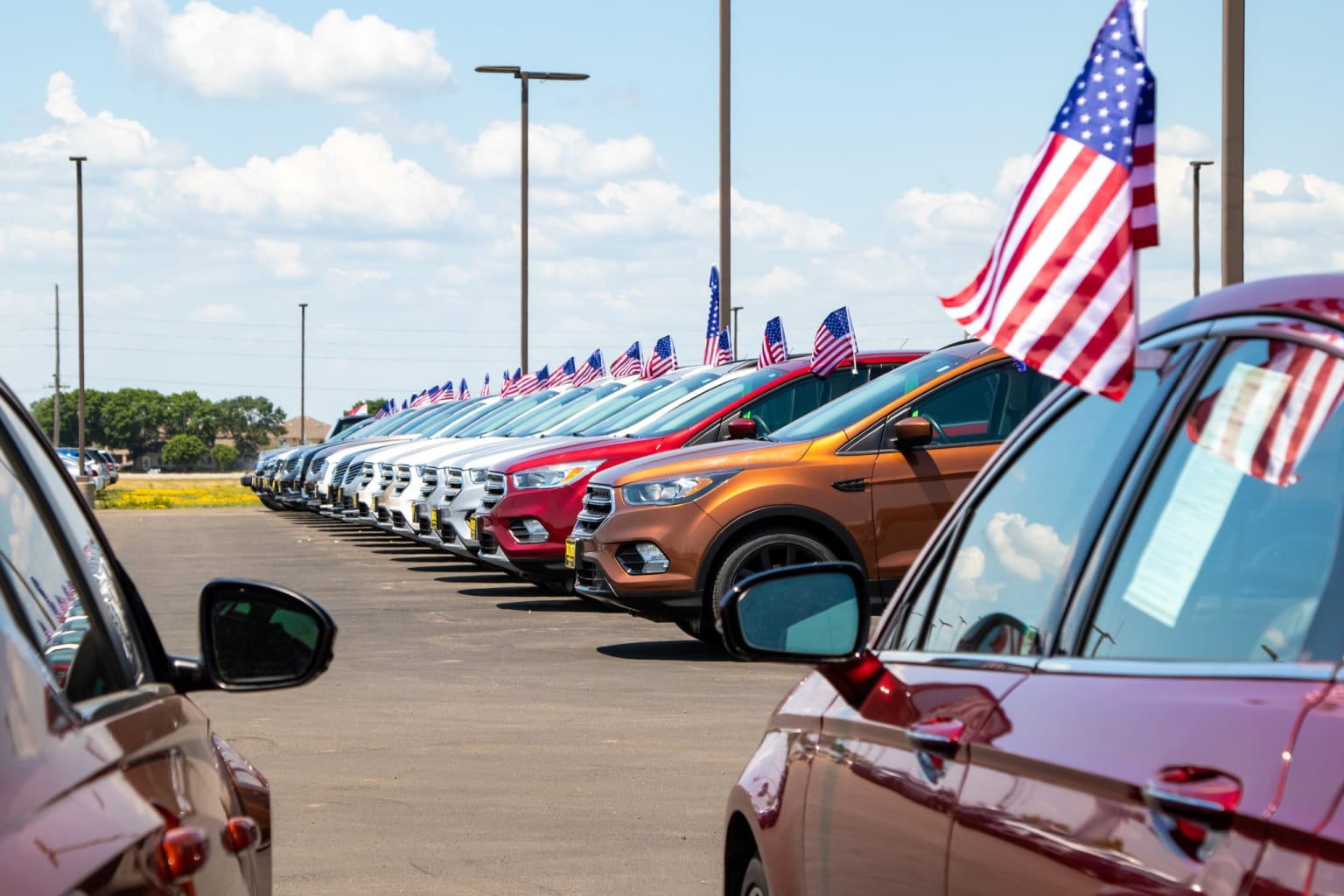 a row of cars parked in a parking lot with american flags on the side of the cars in front of them