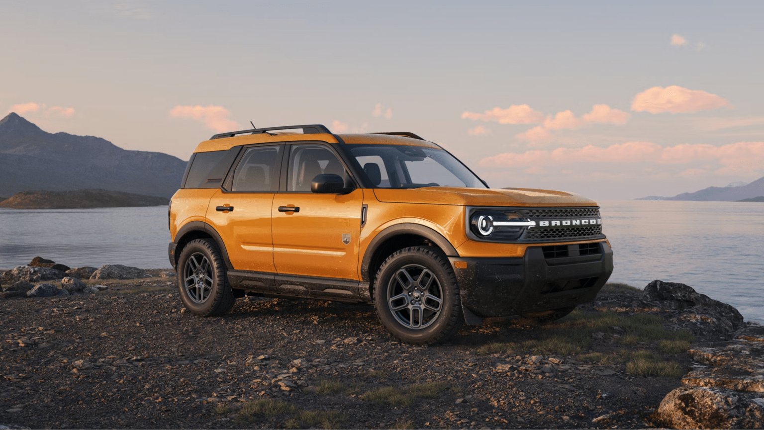 A yellow compact SUV is parked on a rocky cliff overlooking a calm lake and distant mountains under a soft sunset sky.