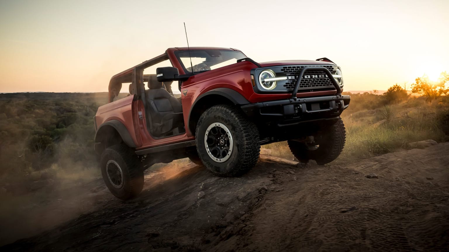 a red truck driving down a dirt road in the middle of the desert at sunset or sunrise or sunset