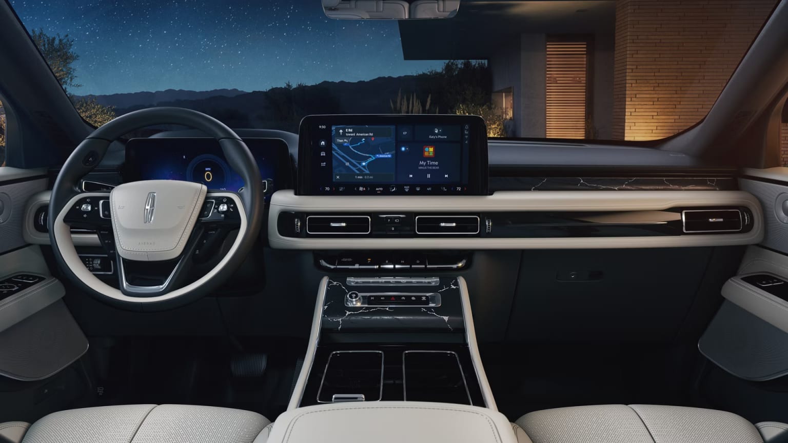 The interior of a modern, high-tech vehicle with a large touchscreen display, steering wheel, and various controls, set against a backdrop of a nighttime mountain landscape.