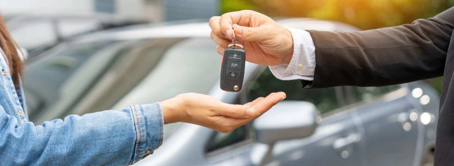Two people exchanging car key in a vehicle-related setting.