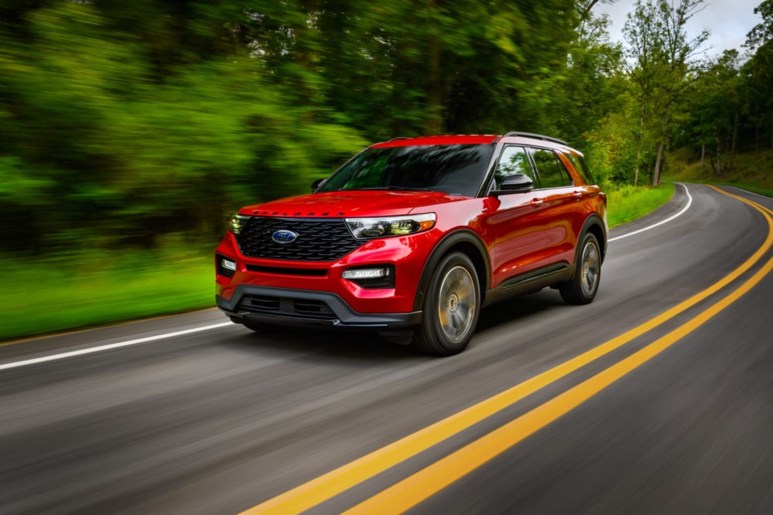 a red ford explorer driving down a road with trees in the background and a blurry picture of the front end of the car