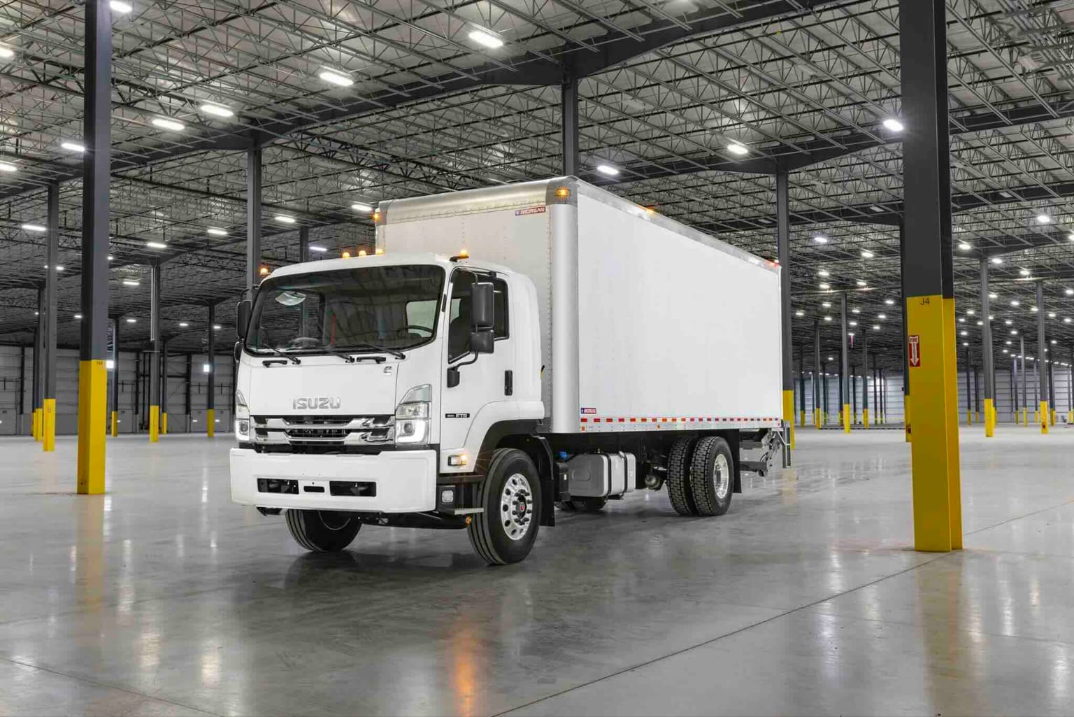 A white box truck parked inside a large, empty warehouse with yellow-striped support columns.