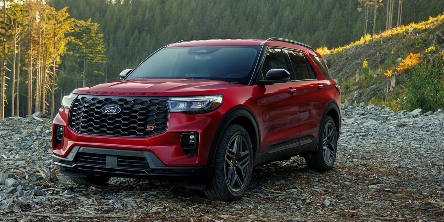 A red SUV is parked on a rocky, wooded hillside with a forest in the background.