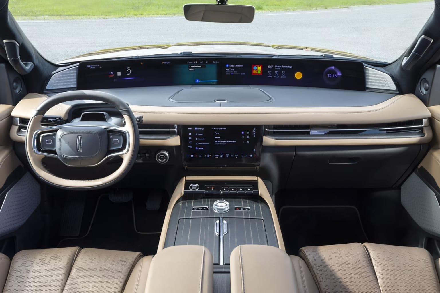 The image shows the interior of a modern, high-tech vehicle with a sleek dashboard, a large central display, and a steering wheel with various controls. The background appears to be a road or driveway, suggesting an outdoor setting.