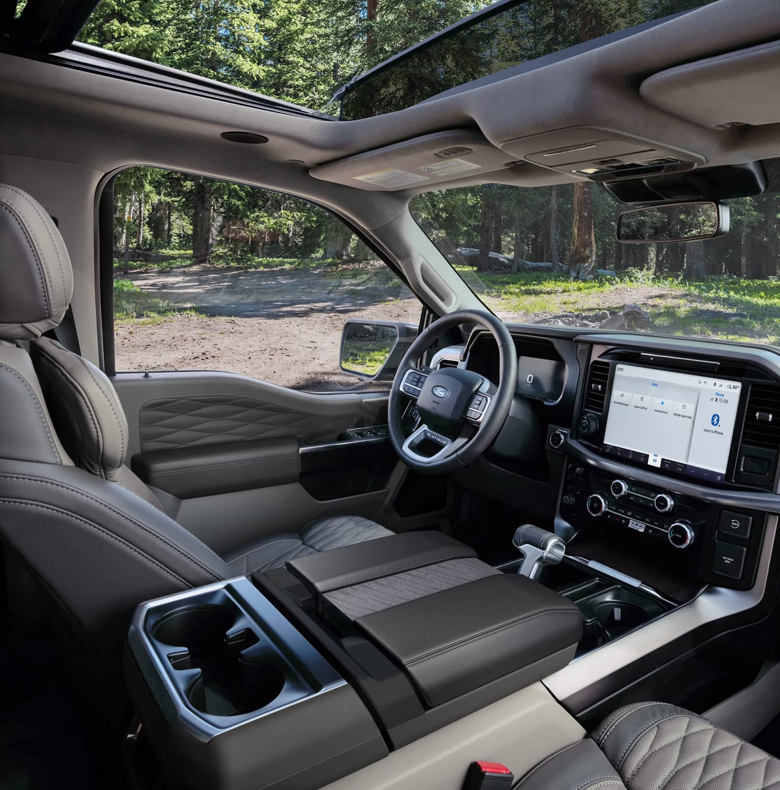Interior of a modern, spacious vehicle with a large dashboard, steering wheel, and seats, surrounded by a lush, forested environment visible through the windows.