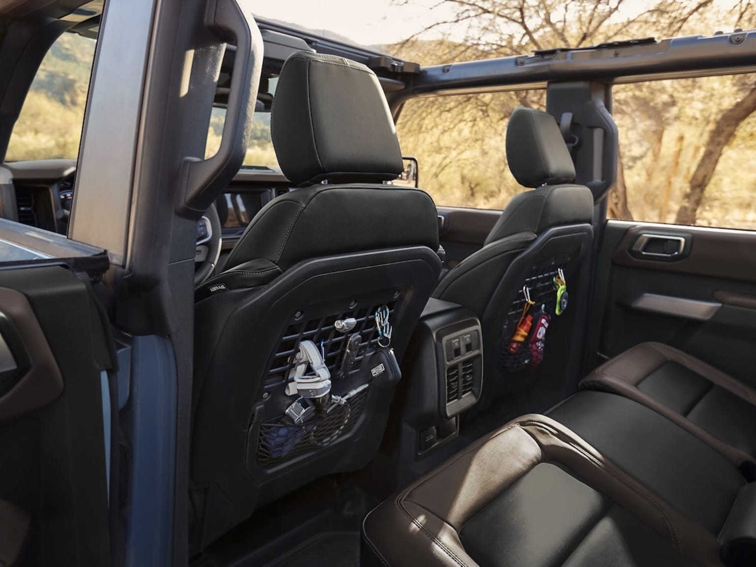 Interior of a vehicle with black leather seats, storage compartments, accessories, and a view of a natural landscape through the windows.