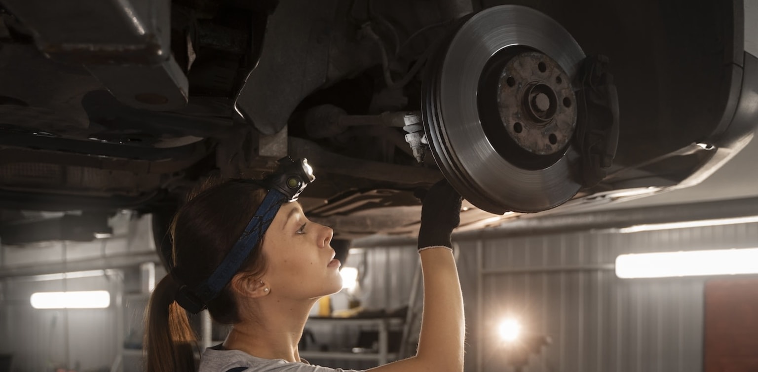 A mechanic's hand working on a brake disc of a vehicle, with various tools and equipment visible in the background.