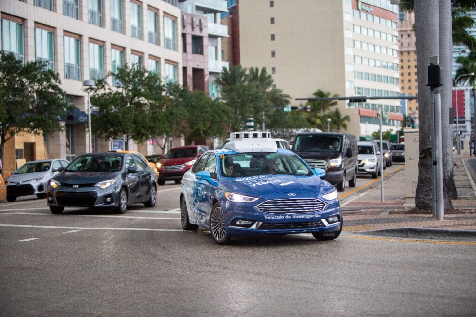 a blue car driving down a street next to a tall building with a traffic light on top of it