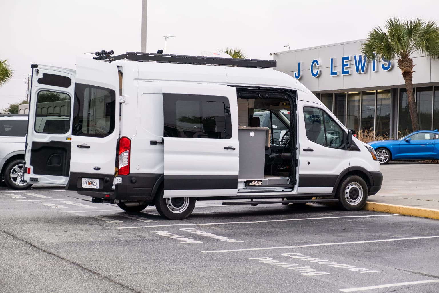 a white van parked in a parking lot next to a blue car in front of a j c lewis store