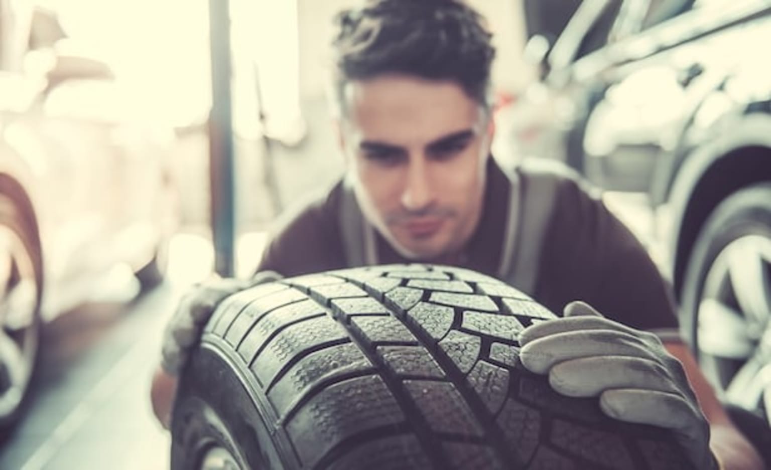 a man working on a car tire in a garage with other cars in the background and a man looking at the tire
