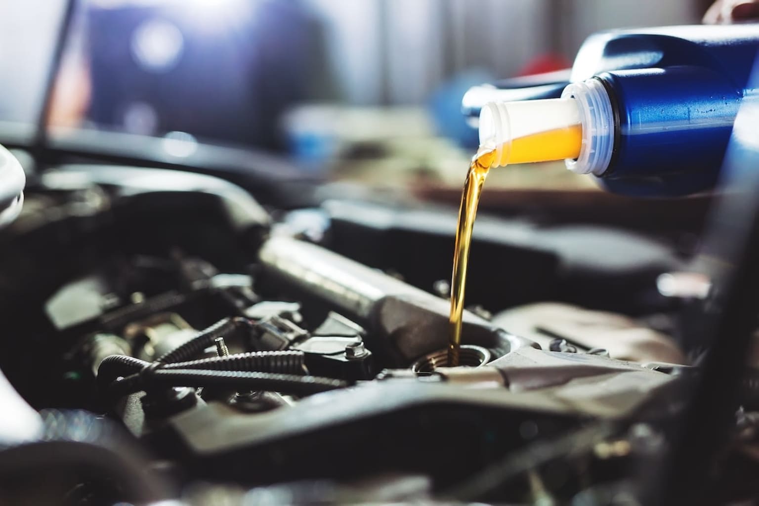 a close up of a car engine with oil pouring out of the top of the engine and a laptop in the background