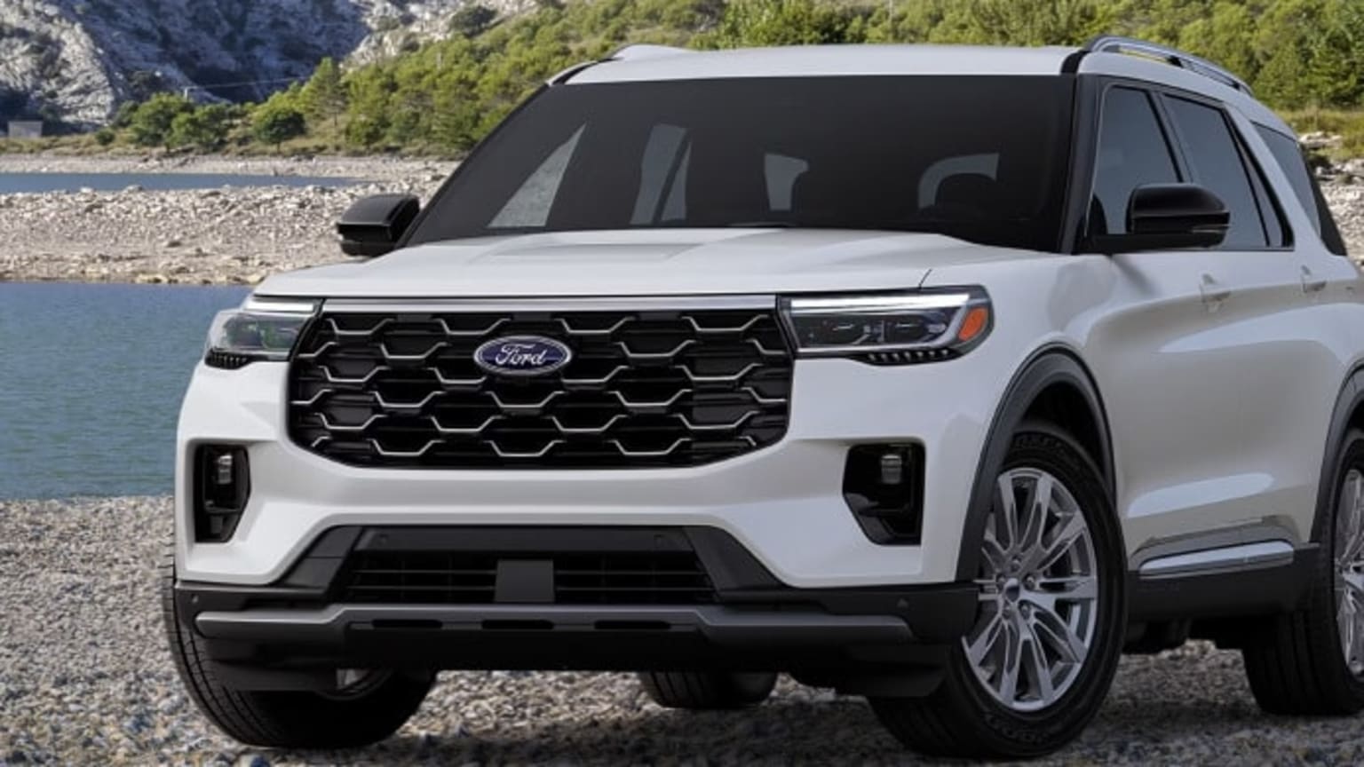 SUV parked on a rocky shore with a body of water and mountains in the background.