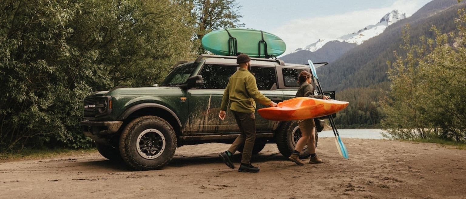 Off-road vehicle with a kayak on roof in scenic outdoor setting.