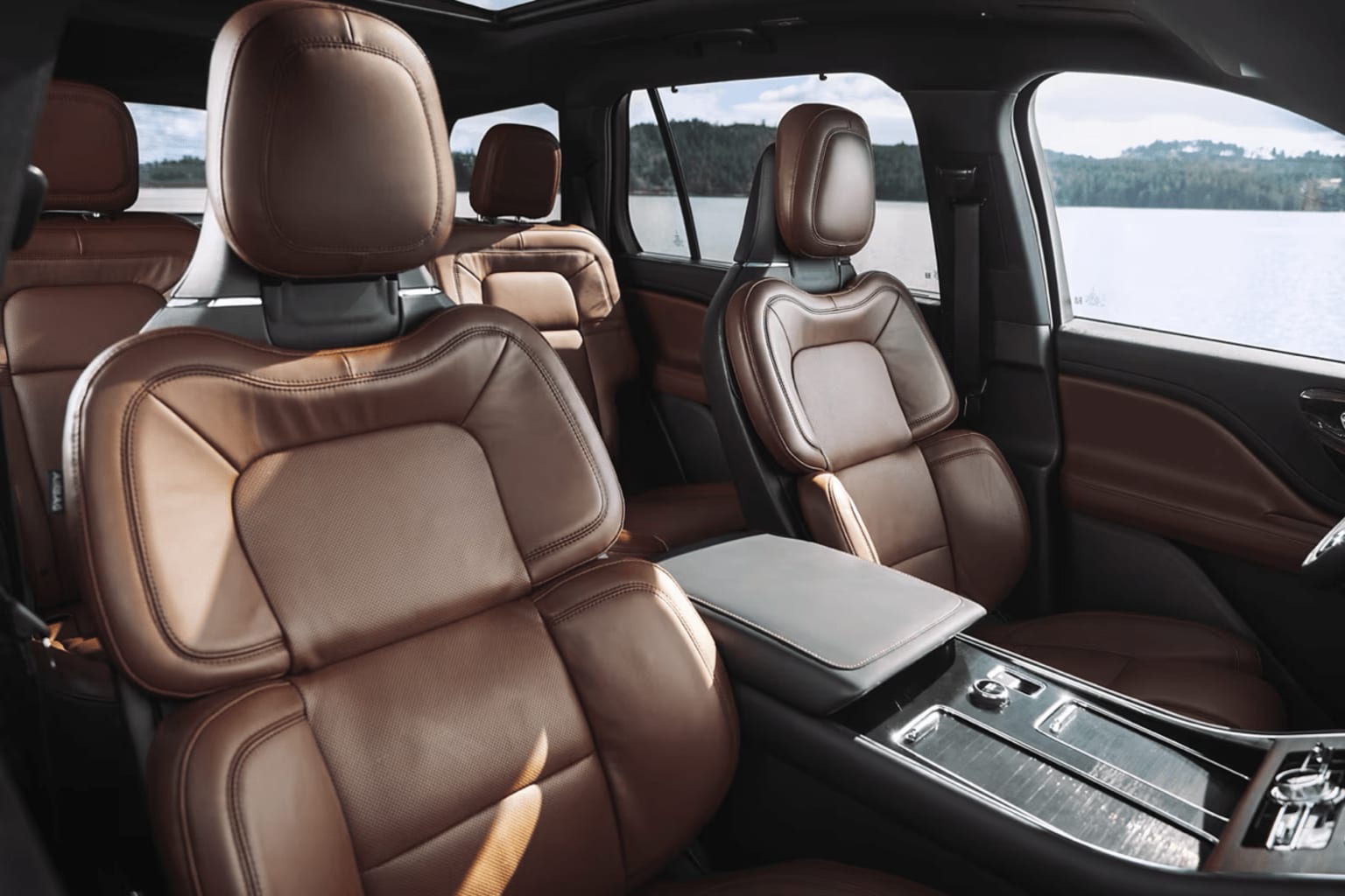 Interior of a luxury vehicle with plush leather seats and a center console, parked in a scenic landscape.
