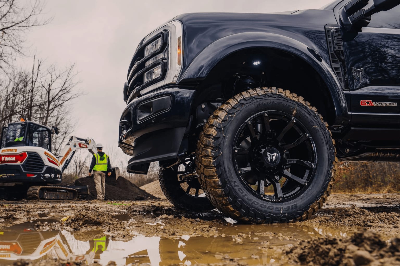 Two rugged off-road vehicles with oversized tires in a muddy, wooded area.