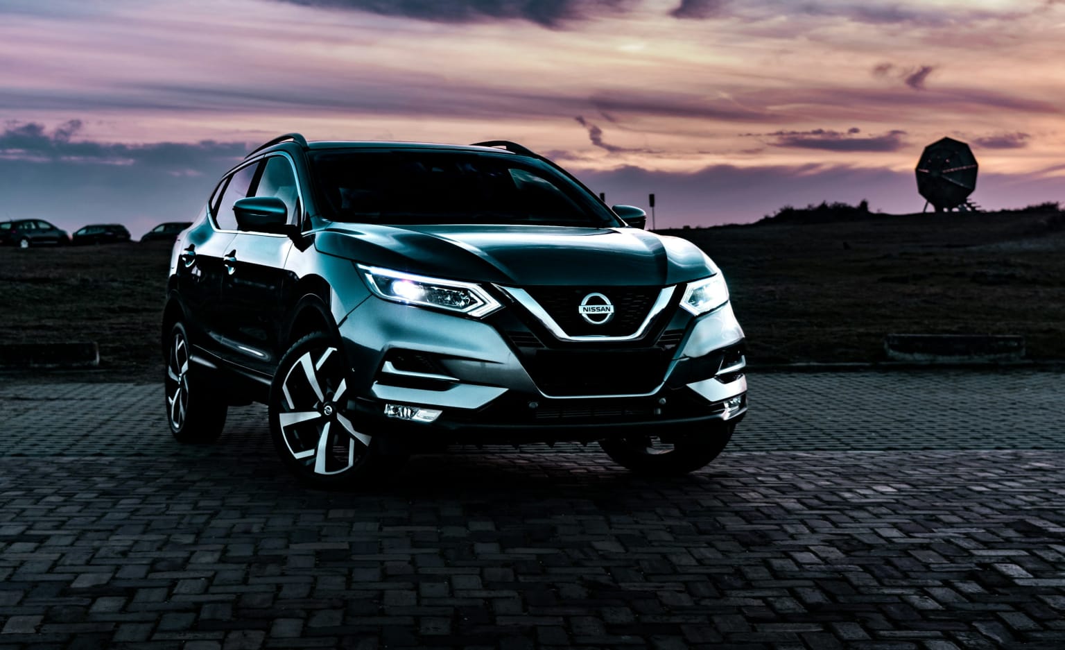 The image shows a sleek and modern SUV parked on a paved surface, with a dramatic sky filled with clouds in the background, creating an atmospheric and visually striking scene.