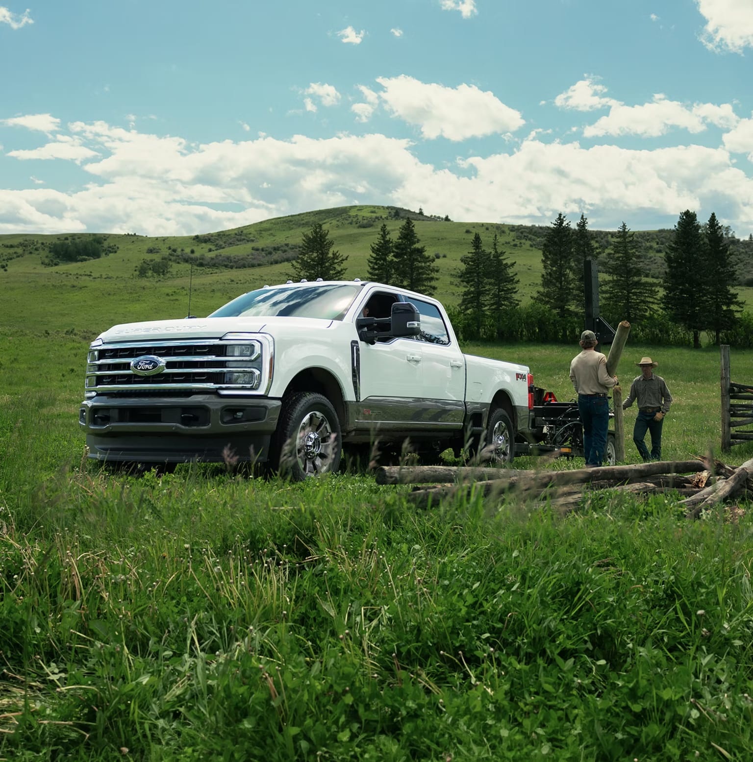 A white pickup truck in a field with two men, green hills, and a cloudy sky.