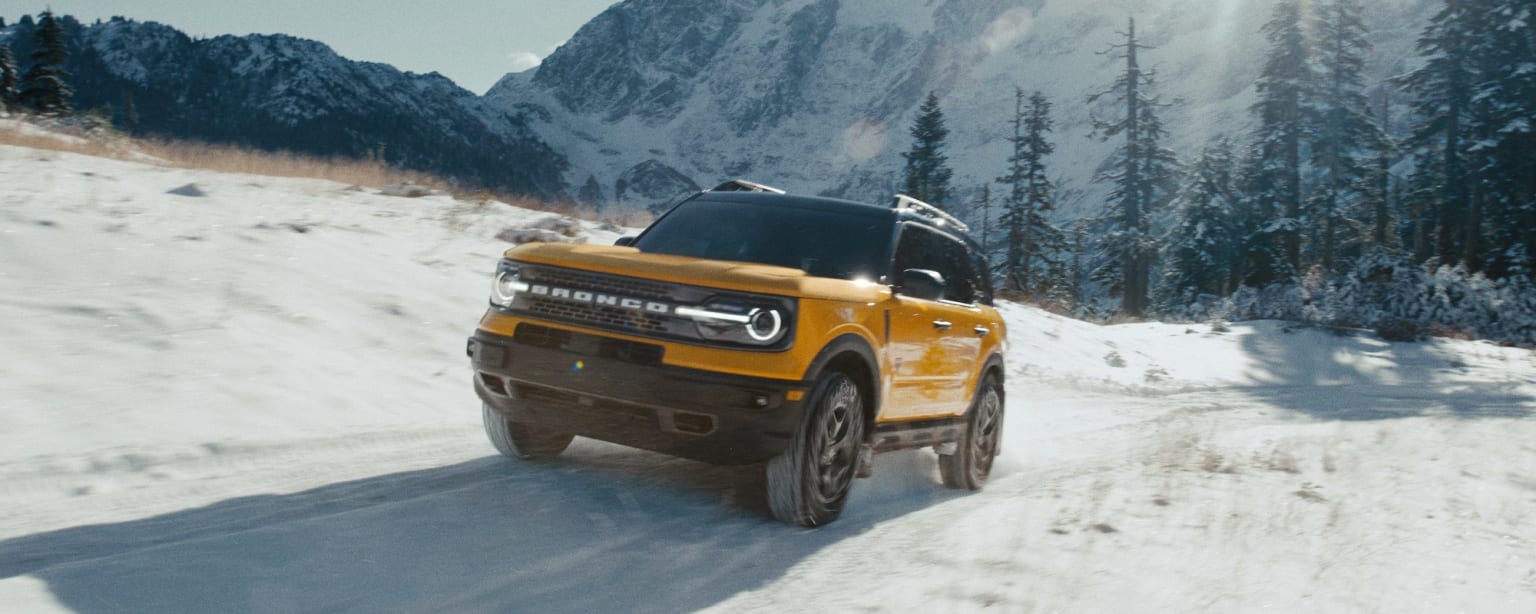 a yellow truck driving down a snow covered road in front of a snowy mountain covered with trees and snow