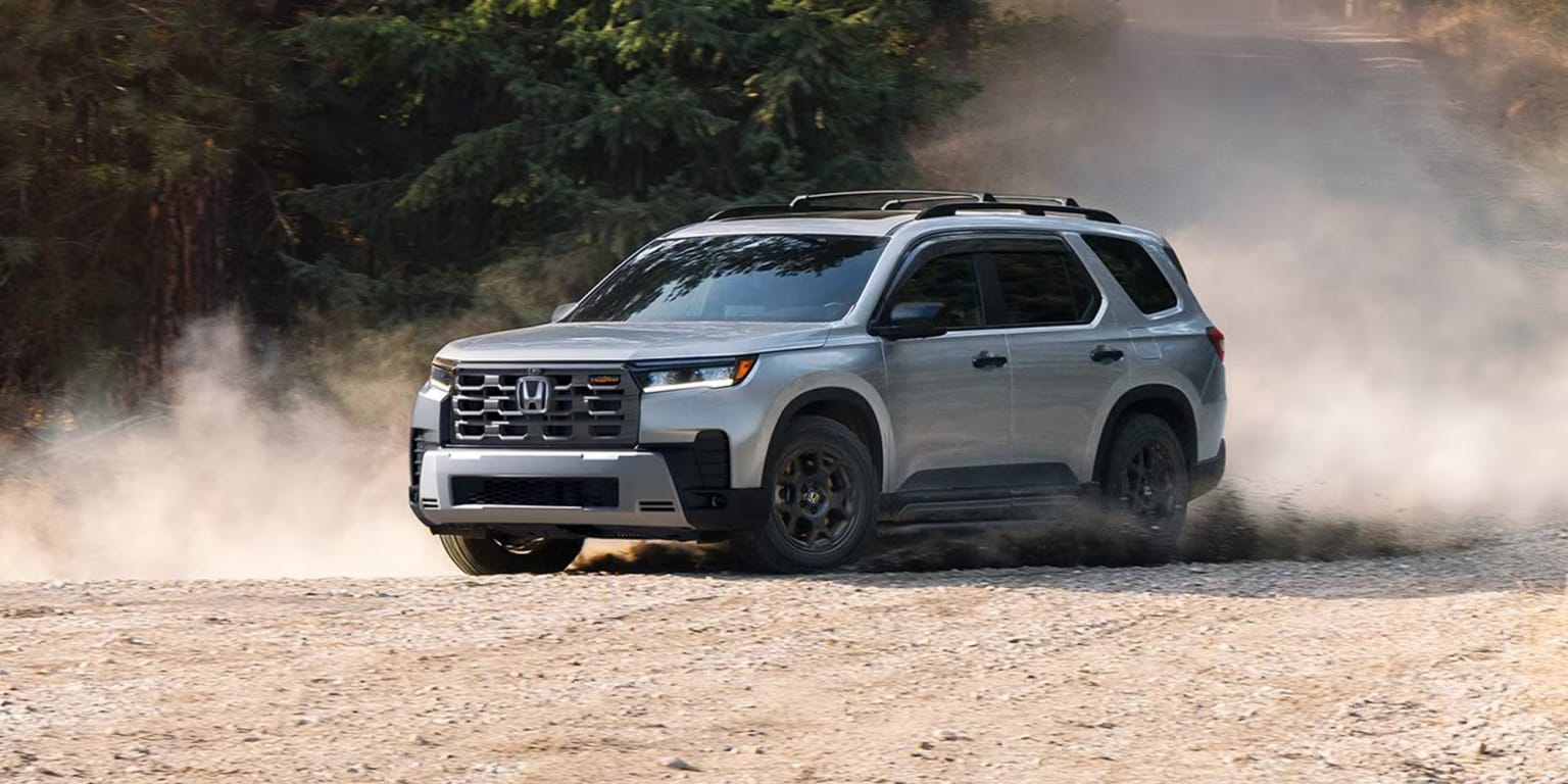 Silver SUV driving on a dirt road with trees in the background.
