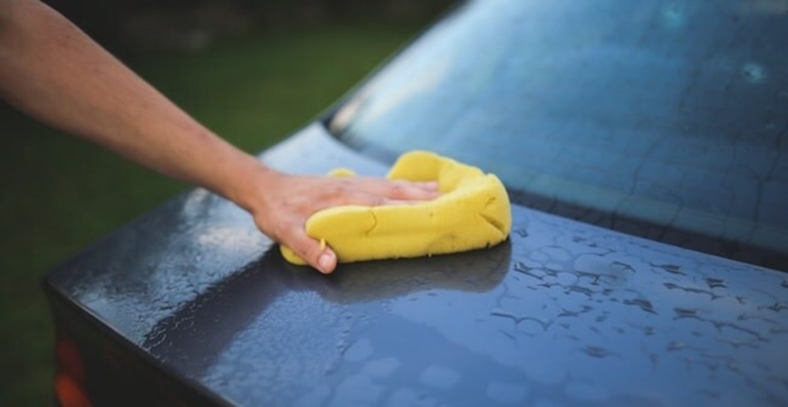 a person is cleaning a car with a yellow microfibre duster on the hood of the car