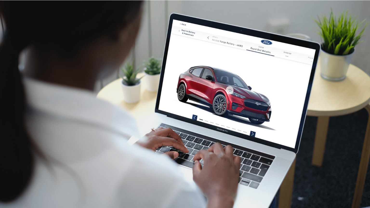 a woman using a laptop with a picture of a car on the screen and a plant on the side of the laptop