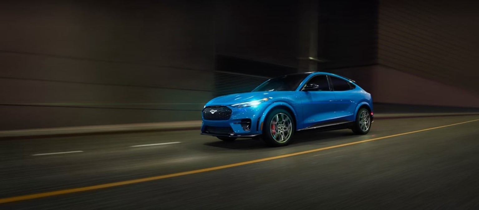 An electric-blue SUV drives through a dimly lit tunnel with its headlights illuminating the path ahead.