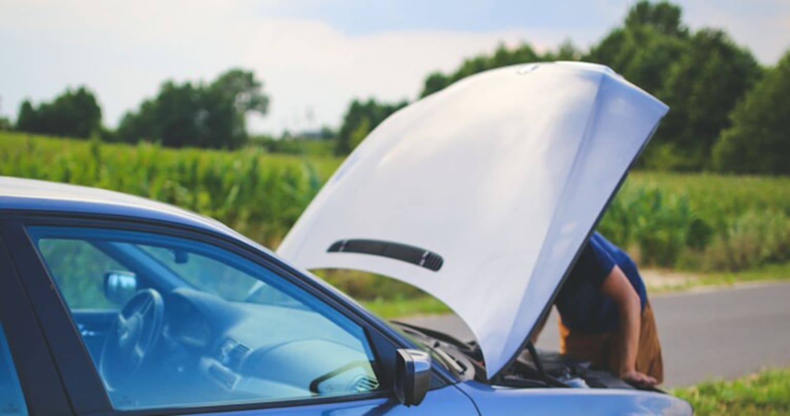 a car that has its hood open on the side of the road with a person leaning out of it