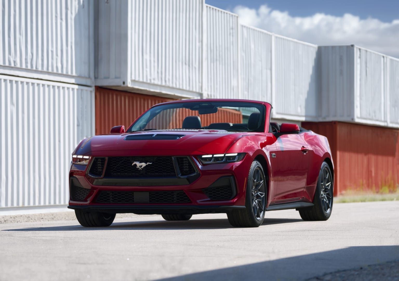 a red sports car is parked in front of a red wall and a white building with a red roof