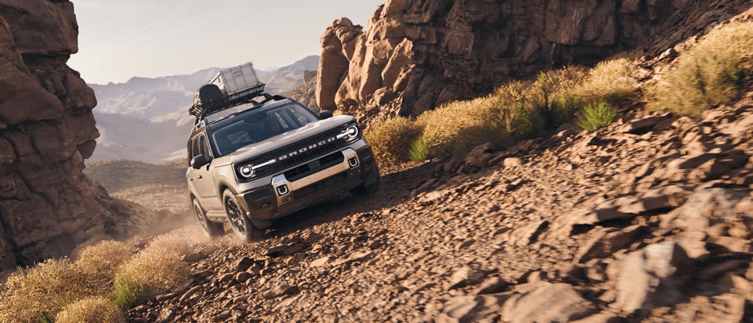 An off-road vehicle navigating a mountain trail with rocky cliffs and an arid landscape.
